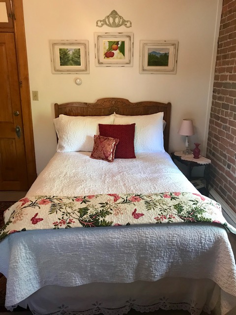 In a cozy guestroom three small pictures hang above a well-made white bed with red accent pillows 